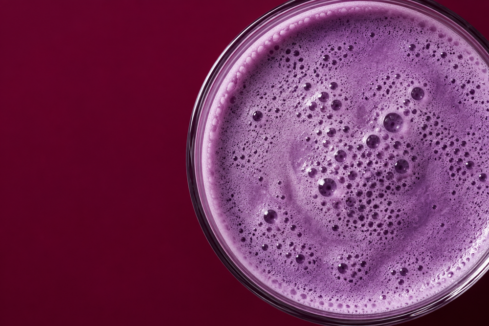 Overhead view of a creamy purple ube drink on a burgundy background