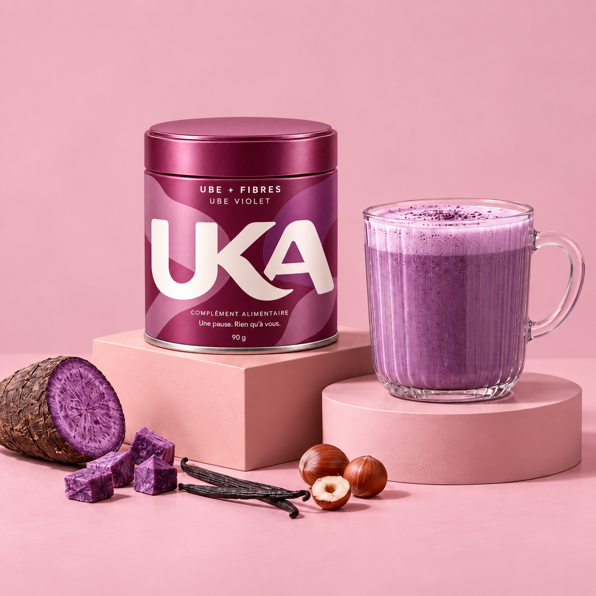 UKA burgundy ube and fiber tin beside a creamy purple drink on blush pink plinths